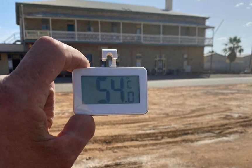 A man holding a thermometer with the reading of 54 degrees celsius.