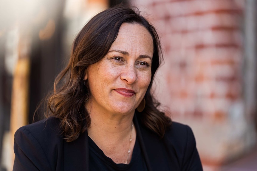 A smiling woman with long, dark hair, wearing a stylish dark outfit.