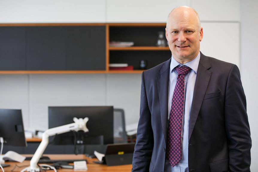 A man in a suit looking into the camera in an office.