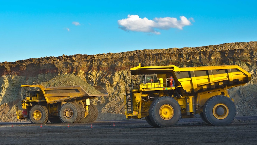 Two large yellow mining trucks on a road in a coal mine