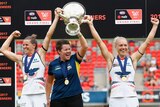 AFLW Crows coach Bec Goddard with the captains holding up the 2017 premiership trophy in 