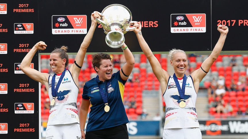 AFLW Crows coach Bec Goddard with the captains holding up the 2017 premiership trophy in 