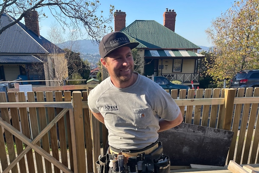 Male builder standing in the front yard of a house with a new picket fence behind him.