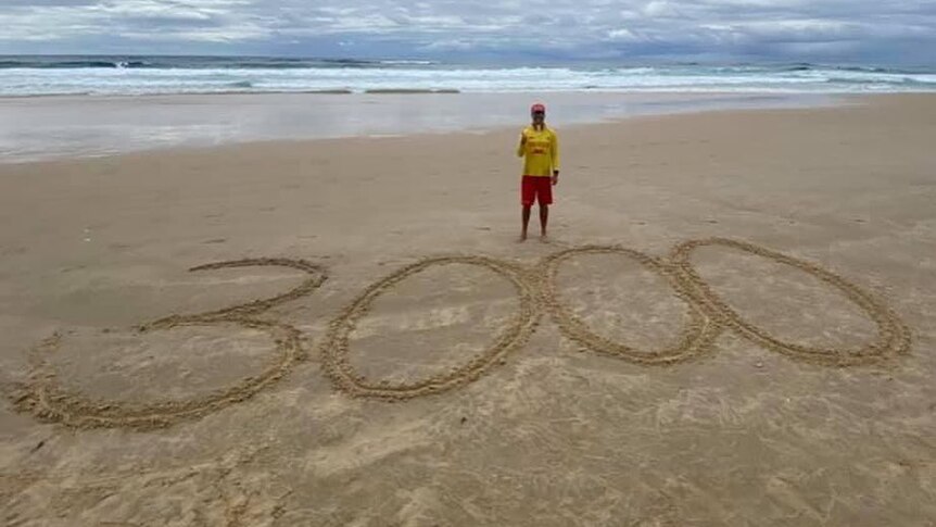 Calan standing on a beach with 3000 drawn into the sand.