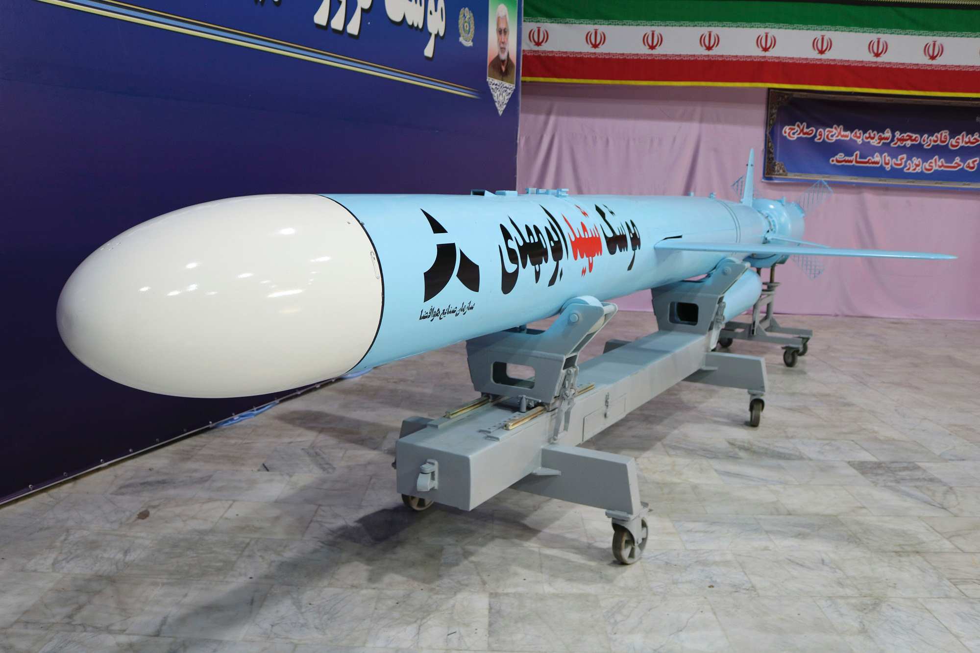 一枚浅蓝色导弹展示在带有阿布·马赫迪 (Abu Mahdi) 图片的蓝色横幅前。