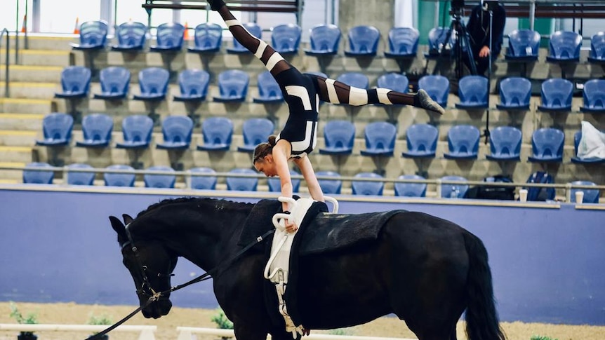 A girl performing a handstand and splits whilst riding a horse