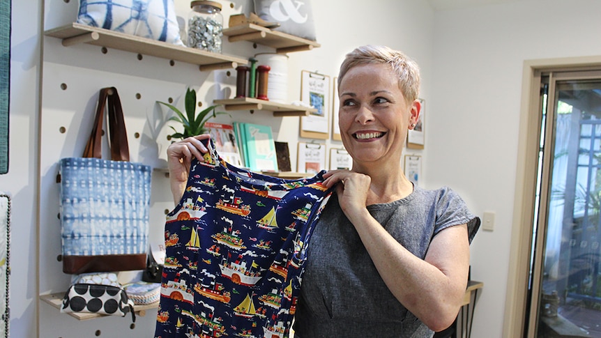 Sewing student Jenni Langan holding up a blue and red tug boat print dress in a craft workshop