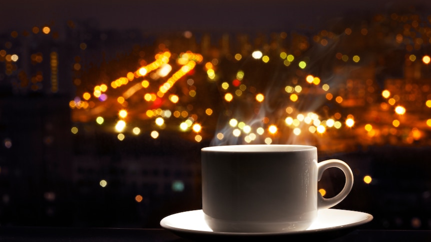 A cup of coffee in a window against the background of city lights