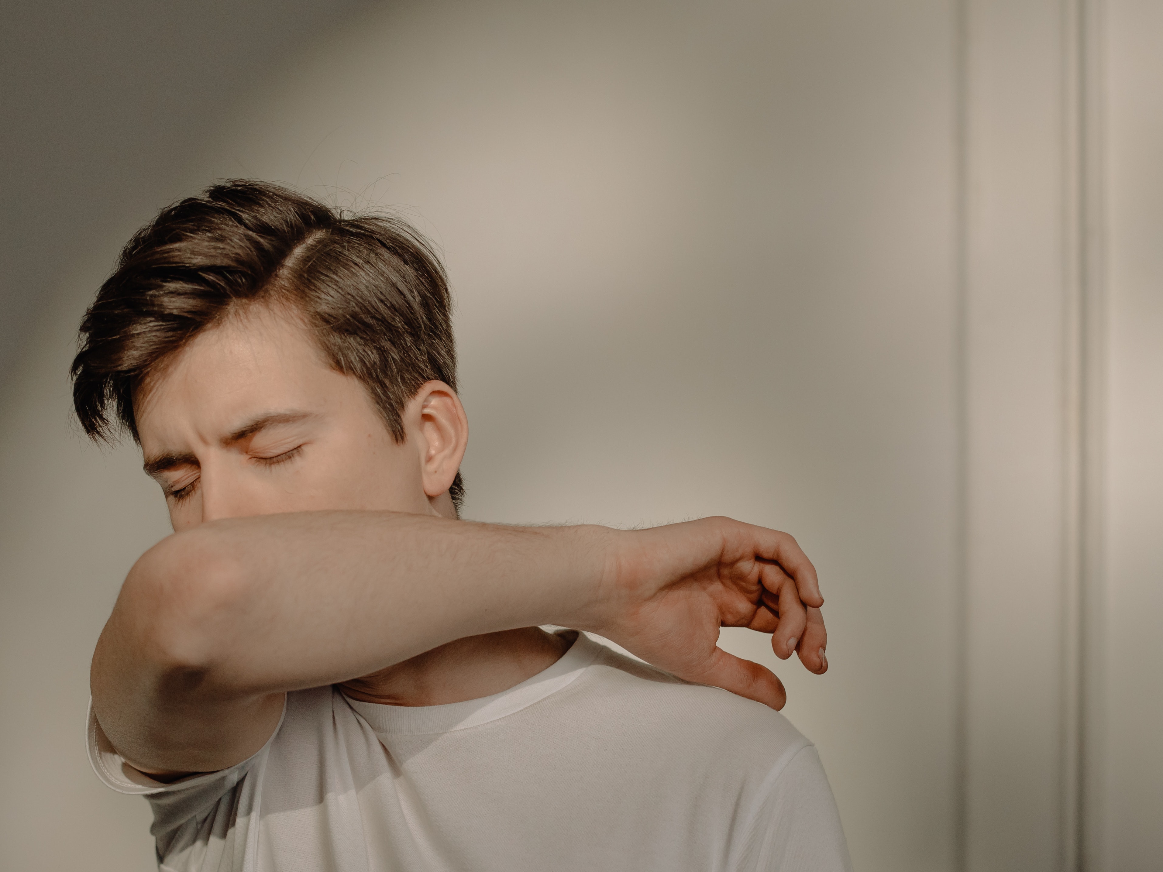 Man in white shirt coughing or sneezing into elbow with white background