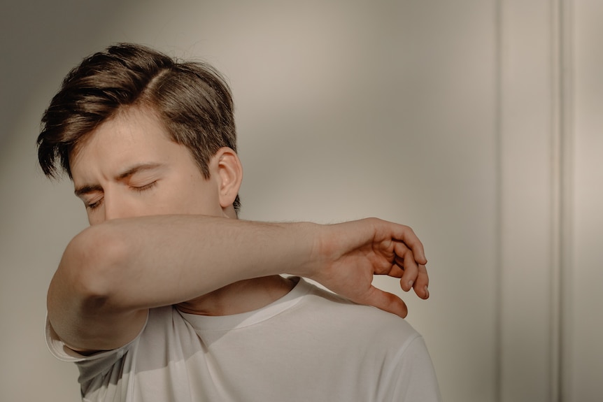 Man in white shirt coughing or sneezing into elbow with white background