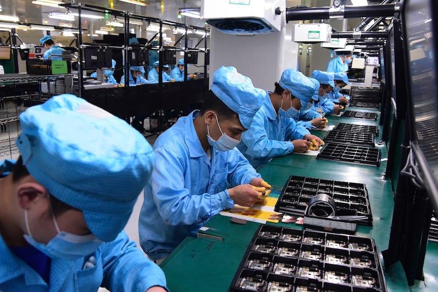 Workers wearing masks labour at a factory for Chinese telecommunications company OPPO.