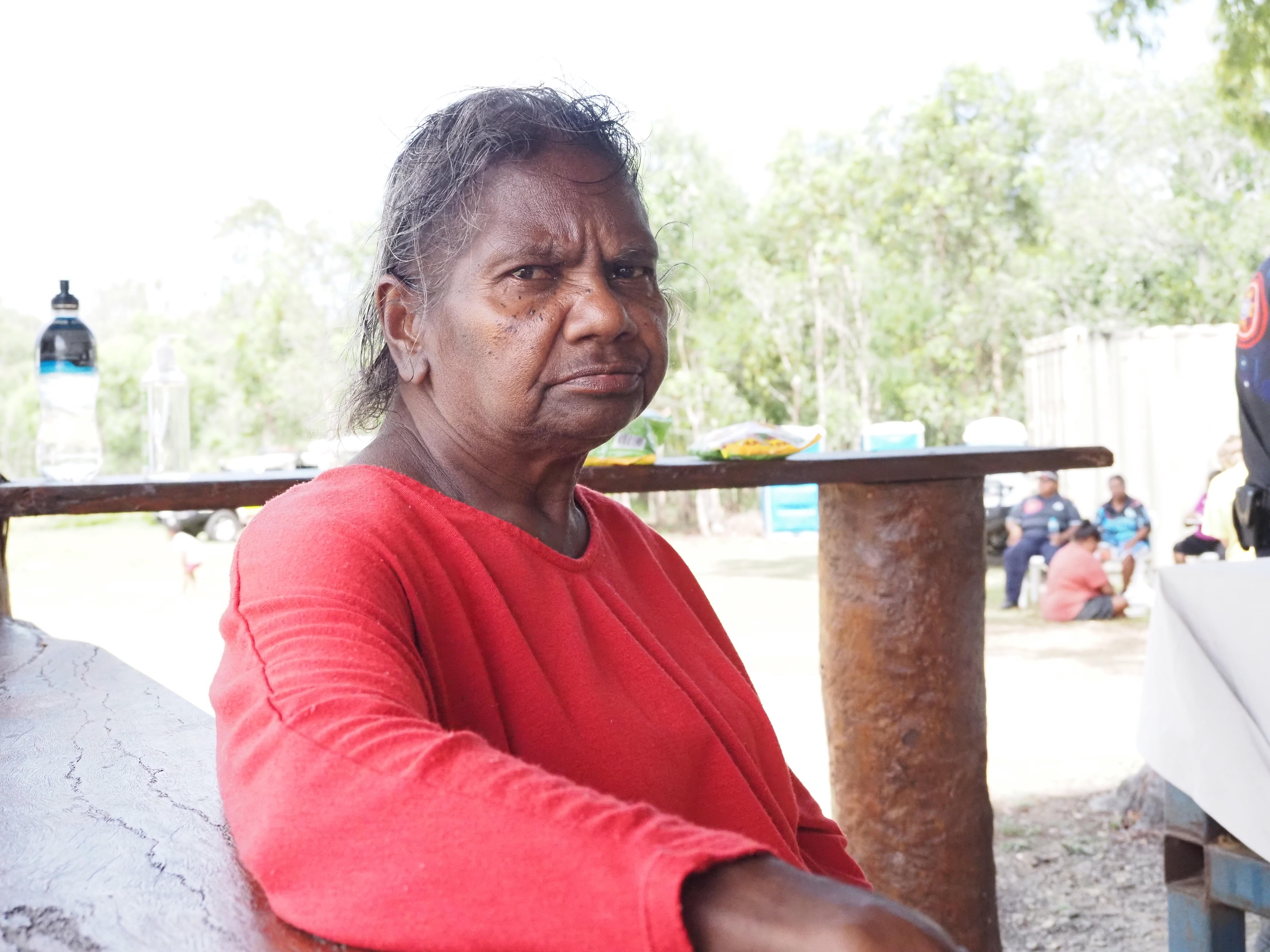 An older Indigenous woman in bright clothes sitting outside.