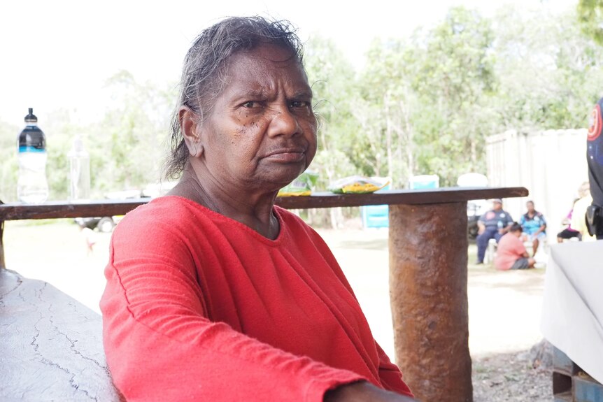 An older Indigenous woman in bright clothes sitting outside.