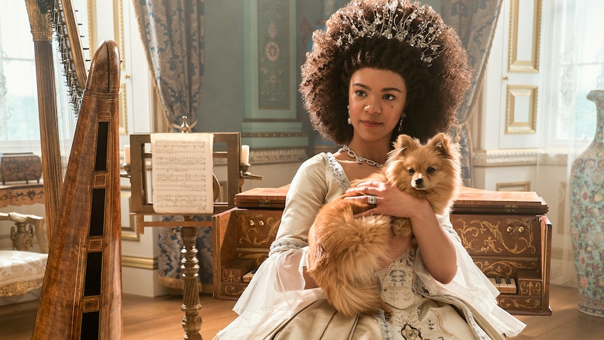 Bridgerton's Queen Charlotte sits in a beautiful room, clutching a very fancy dog.