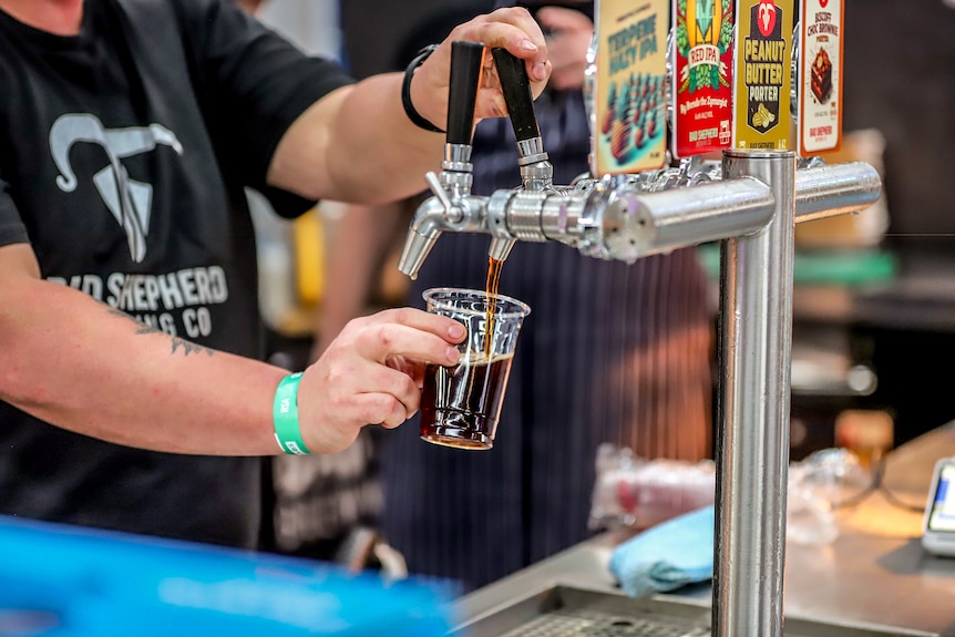 Brown craft beer poured from a silver beer tap by man wearing black t-shirt