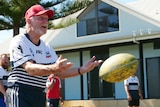 A man with a red cap throwing a rugby ball outside of a building with his team mates standing around him.