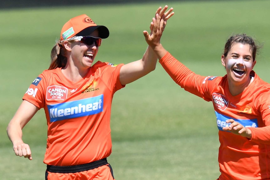 Two smiling female cricketers high five on the field.