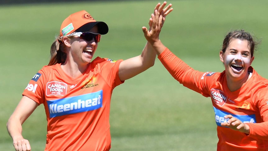 Two smiling female cricketers high five on the field.