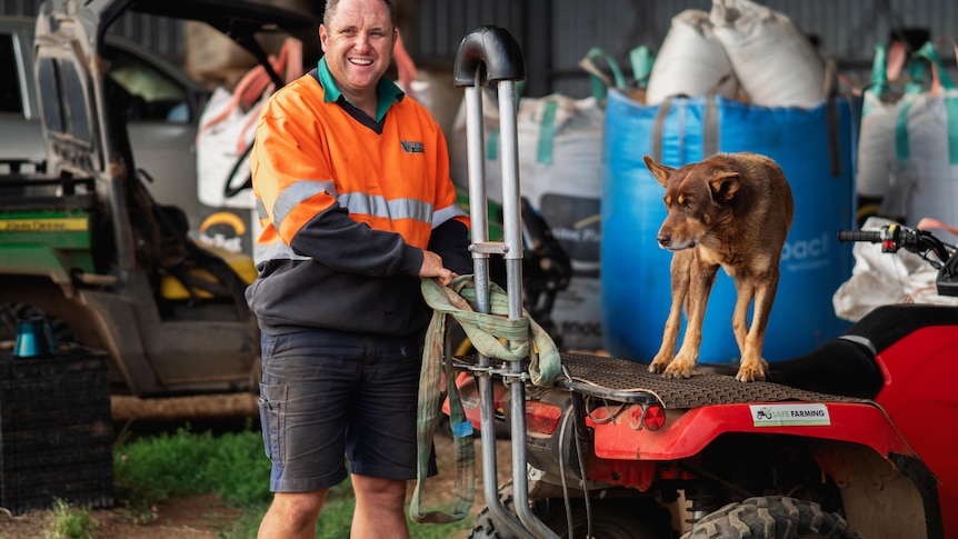 man standing behind quad bike with dog on the seat