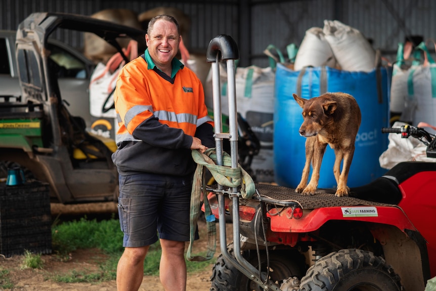 man standing behind quad bike with dog on the seat