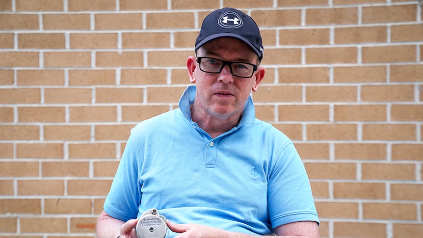 Mathew Kennedy holds a medical pump, which looks a bit like a hockey puck, over his stomach where the device once sat.