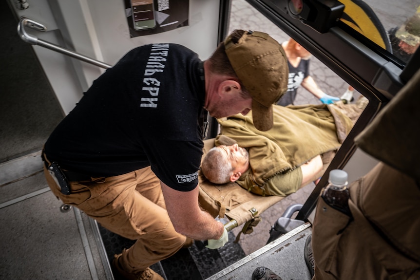 A man on a stretcher is carried up the narrow bus steps