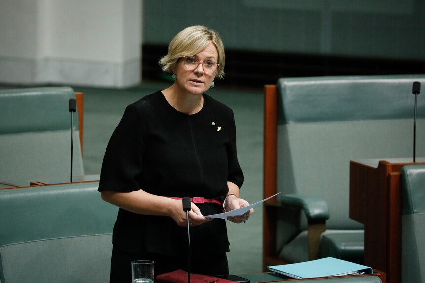 Steggall is standing, wearing black, holding papers, mid-speech