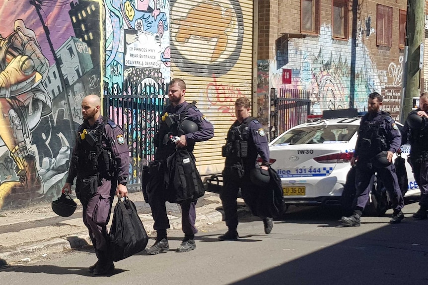 Police in heavy duty uniform carry bags along the street.