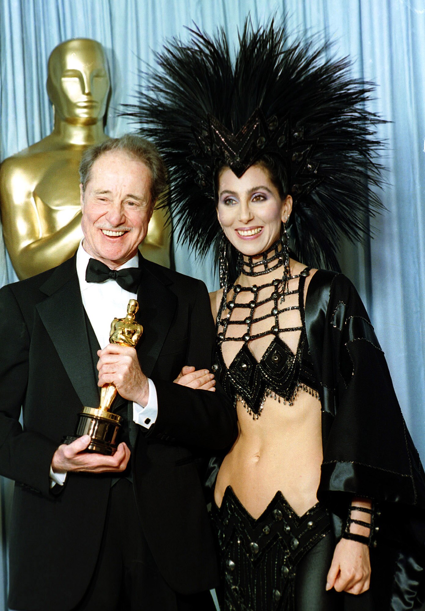 Cher wears a barely-there cut-out black gown with huge black feather head piece.