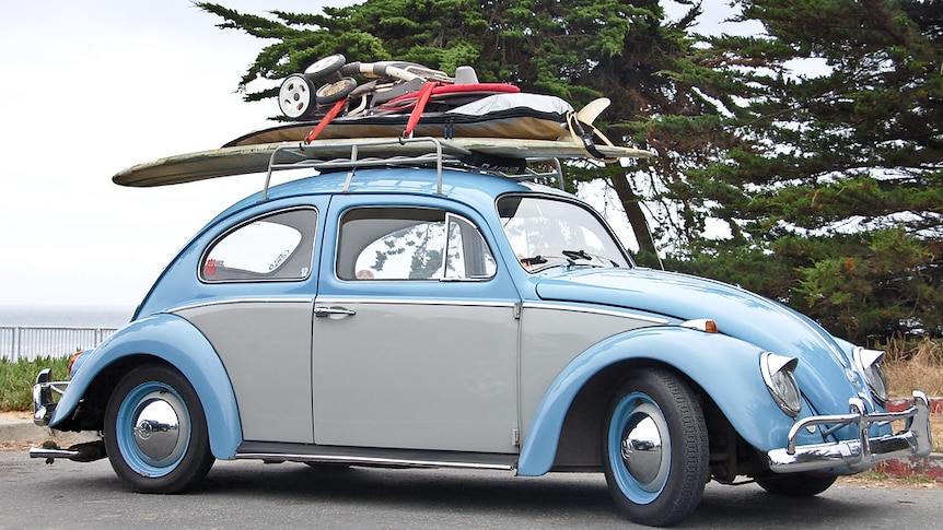 A blue and grey Volkswagen Beetle is pictured with surfboards and pram on its roof.