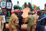 Soldiers unload a coffin from the back of a truck as colleagues stand by holding portaits of the dead