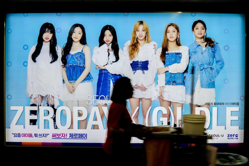 A cleaner walks past a K-pop billboard in Seoul.