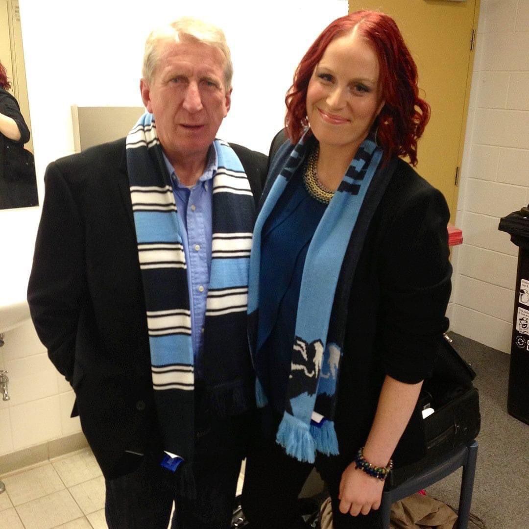 Erin with her dad as an adult in nice clothes and a footy scarf, smiling and standing next to each other.
