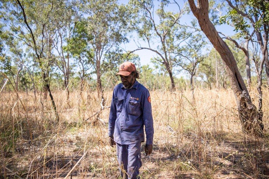 Mimal ranger Anthony Kennedy crosses his arms, tall brown grass and bushland in the background.