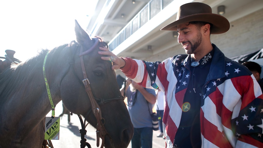 A man in a US flag jacket pats a horse