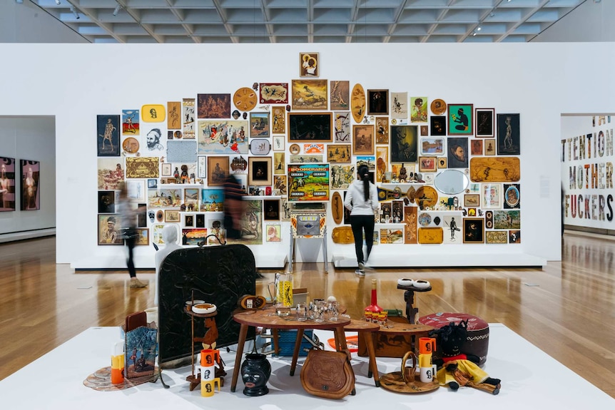 A gallery wall and table covered in mid-century bric-a-brac, covered with stereotypical designs inspired by Aboriginal Australia