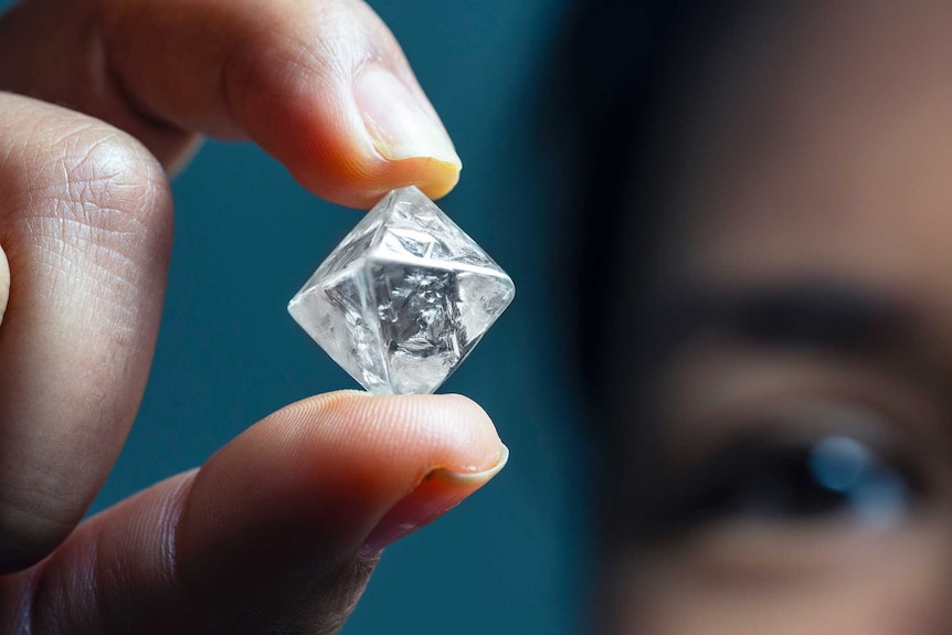 A close up of a cube shaped diamond being held up by a man.