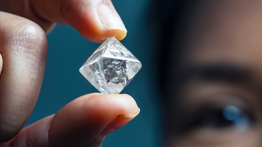 A close up of a cube shaped diamond being held up by a man.