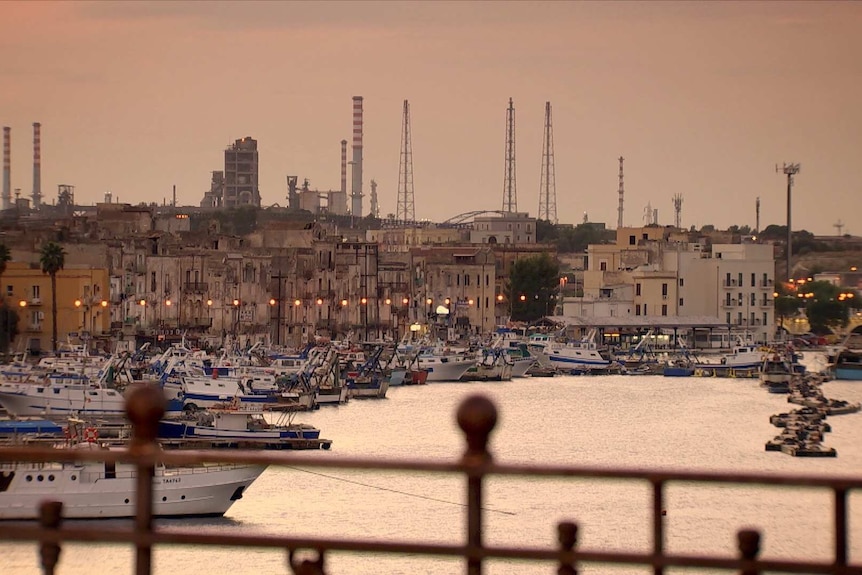 Boats lined up in Taranto's harbour with the steelworks in the background.