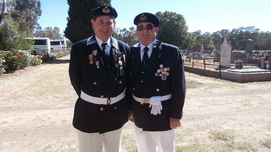 Two men in uniform stand next to each other at cemetery