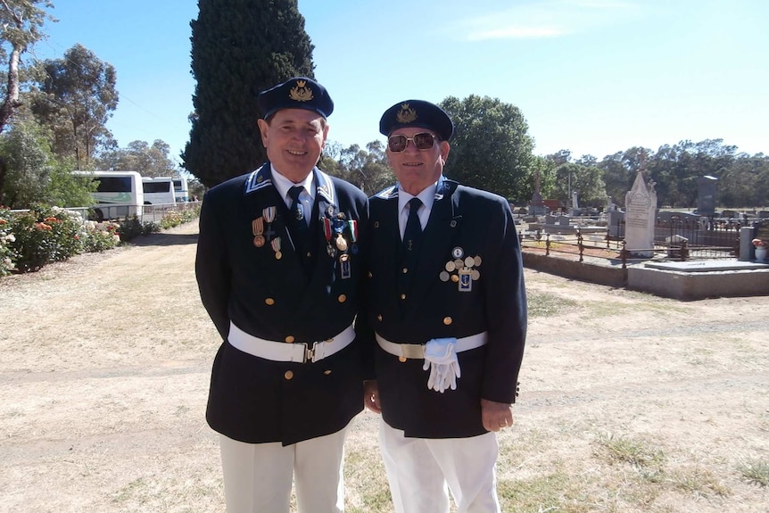 Two men in uniform stand next to each other at cemetery