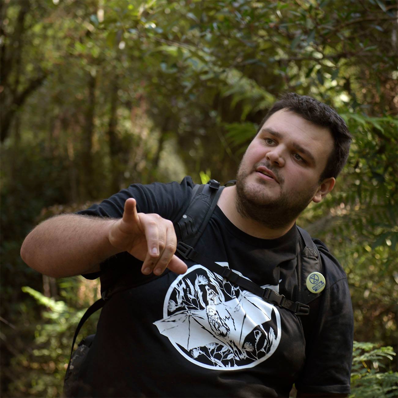 Un hombre con una mochila y una camiseta se encuentra en un bosque.