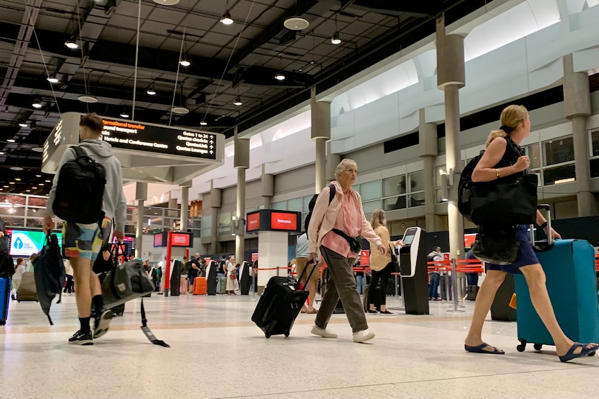 People walking quickly through an airport terminal carrying bags and wheeling luggage