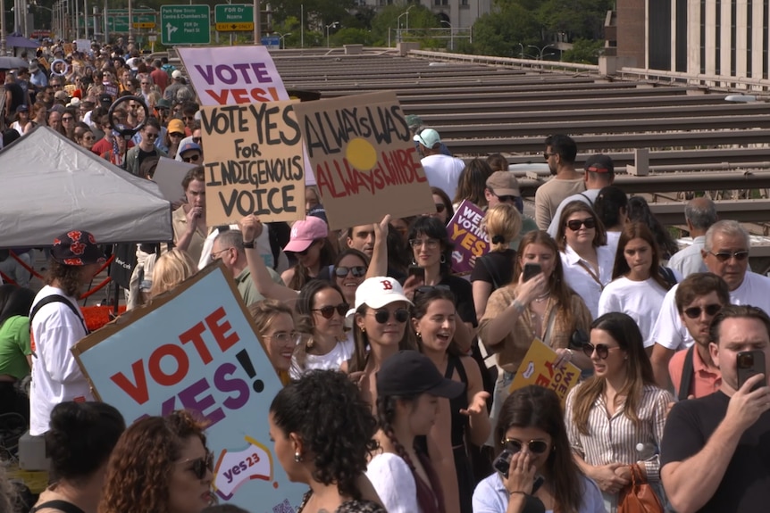 A crowd of people holding signs that say vote yes walking over the Brooklyn Bridge in New York.