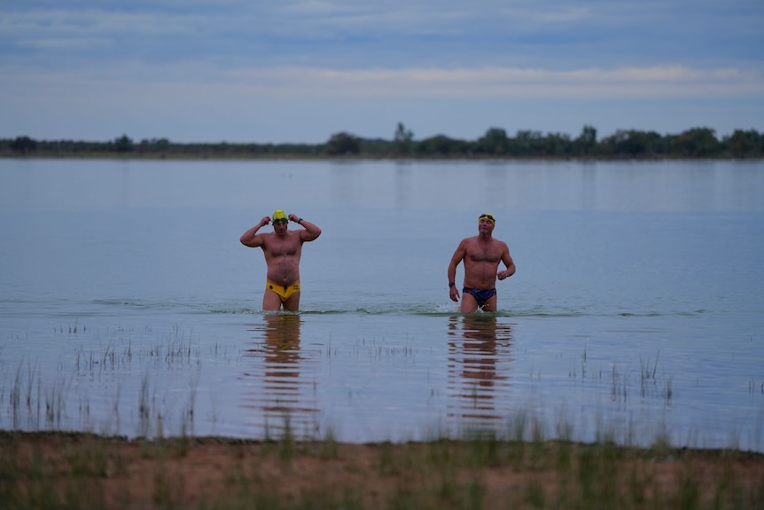 Two men in swimming outfits exit a lake.