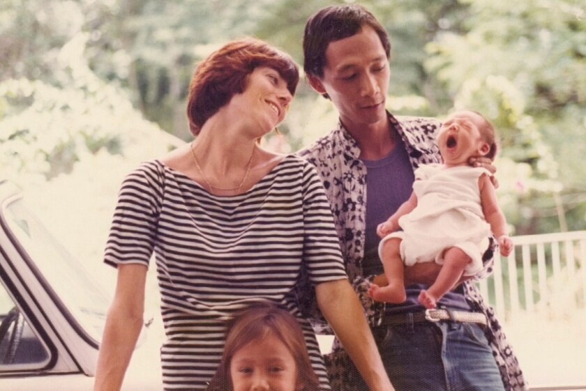 A man holding his newborn baby, while his wife looks on.