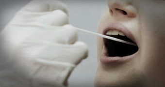 A gloved hand places a swap on an open mouth