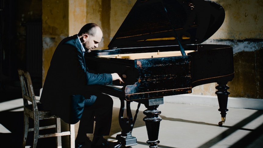 Kirill Gerstein wearing a blue suit, with hands over the piano keyboard