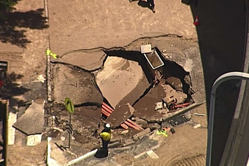 Cracked and sunken pavement and piping visible in the hole.