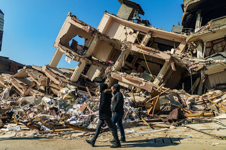 Two men walk past a destroyed building